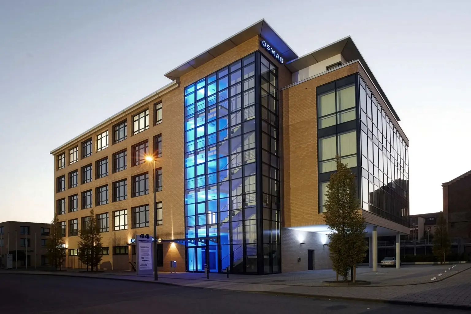 Modernes Bürogebäude mit Glasfassade und blauer Beleuchtung.