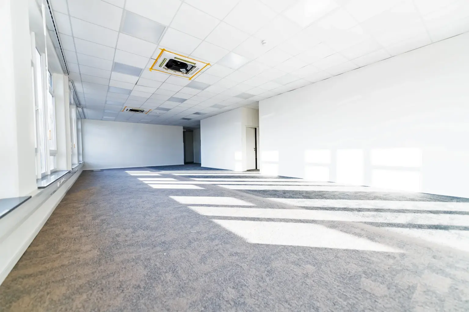 Leerer Büroraum mit großen Fenstern, viel Tageslicht, ideal für Arbeitsplätze.
